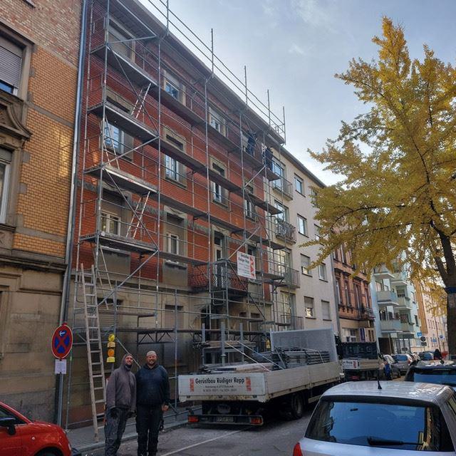 Baugerüst an einem Mehrfamilienhaus. Im Vordergrund zwei Mitarbeiter